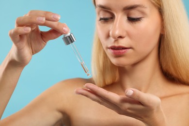 Beautiful woman applying cosmetic serum onto her hand on light blue background