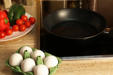 Photo of Many fresh eggs and vegetables near frying pan on wooden countertop in kitchen