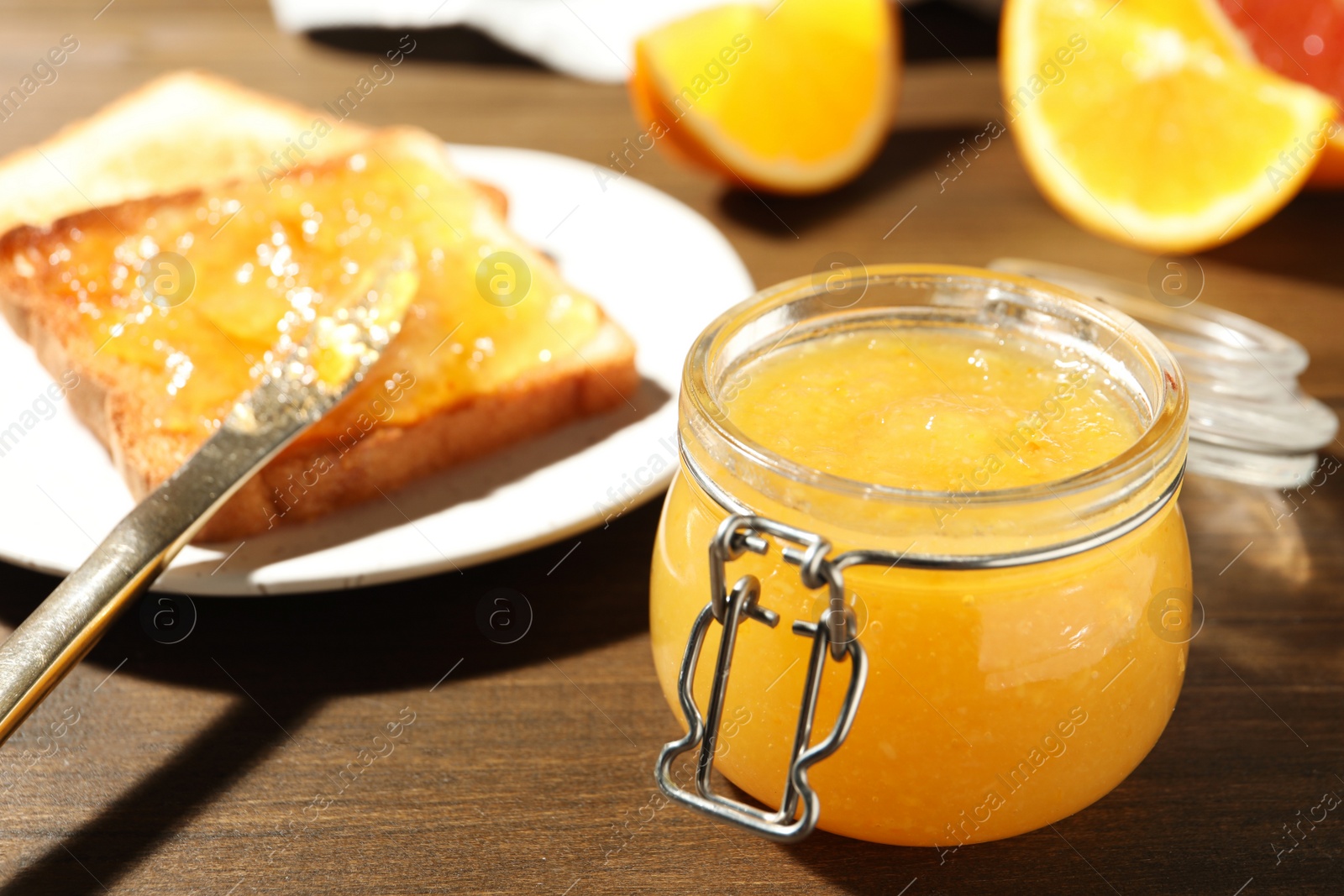 Photo of Delicious orange marmalade and toasts on wooden table