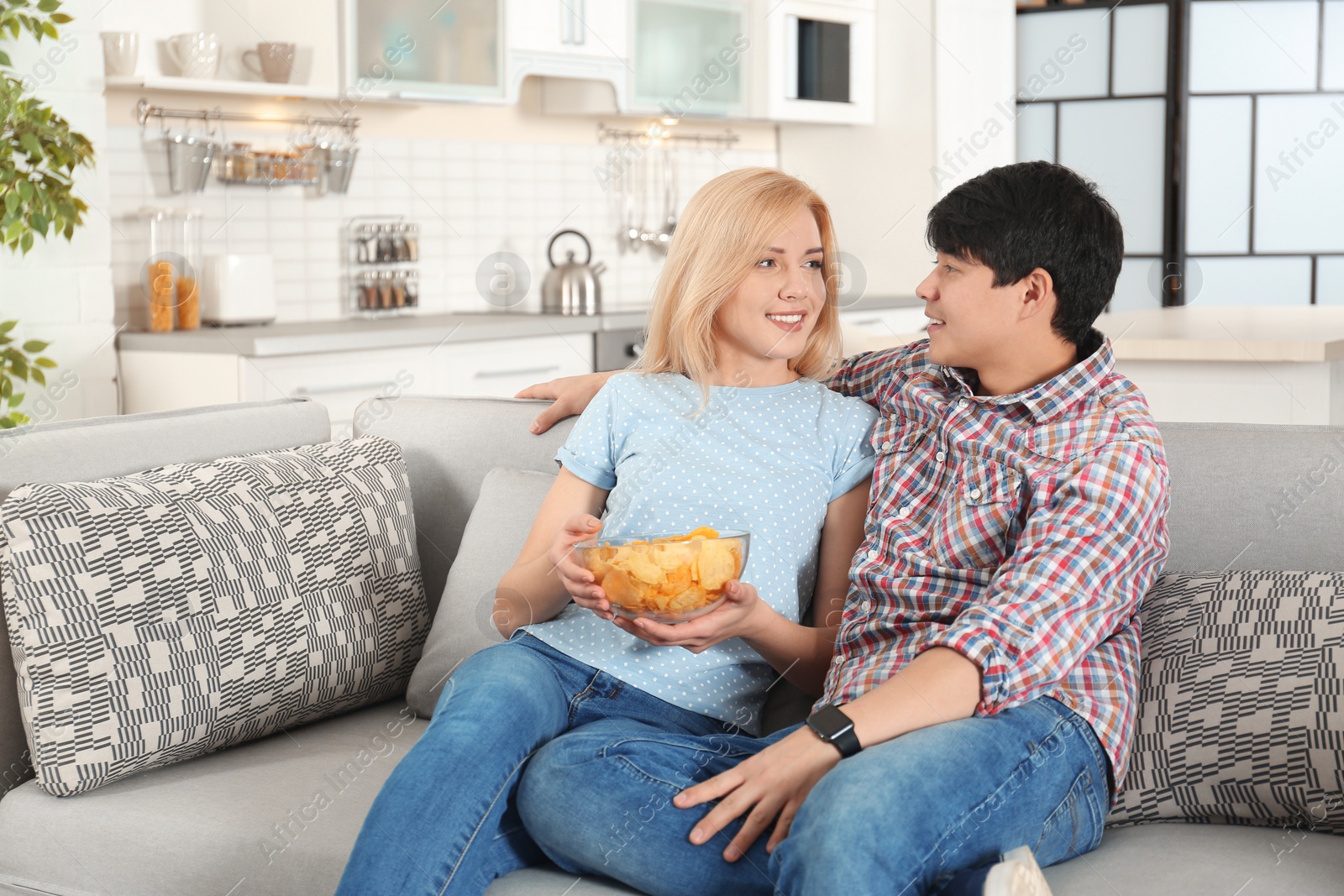 Photo of Young couple with bowl of chips watching TV on sofa at home