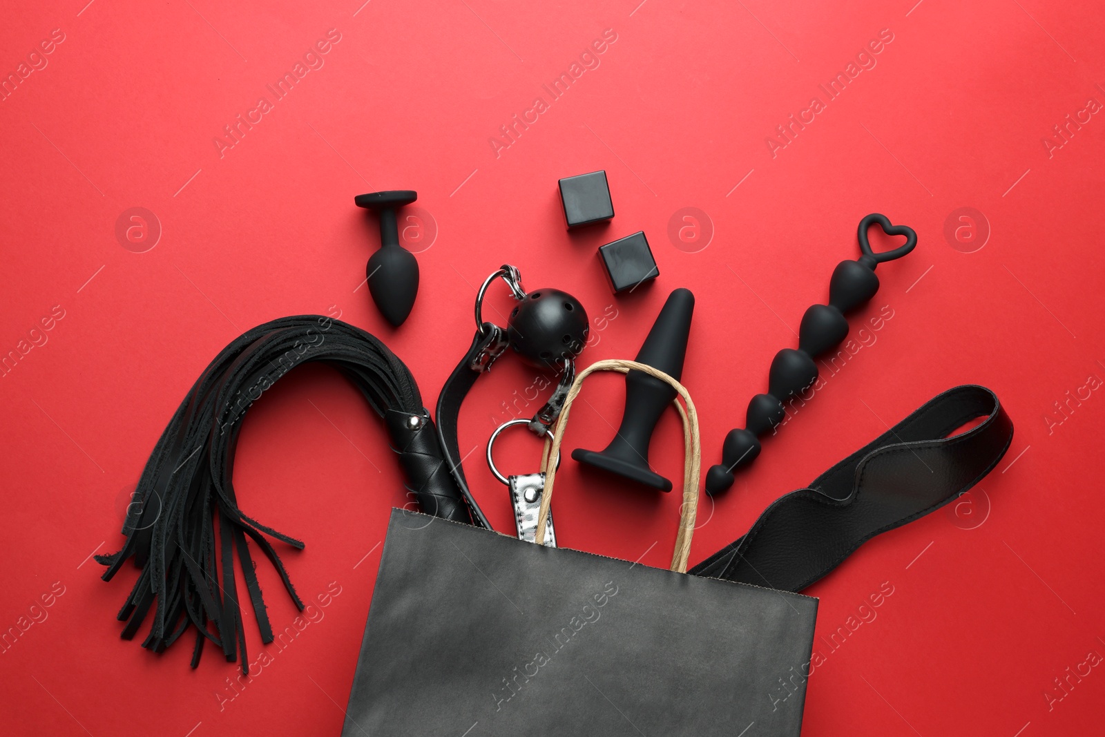 Photo of Shopping bag and different sex toys on red background, flat lay