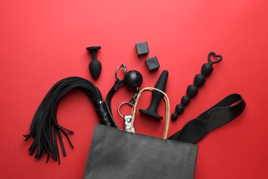 Shopping bag and different sex toys on red background, flat lay