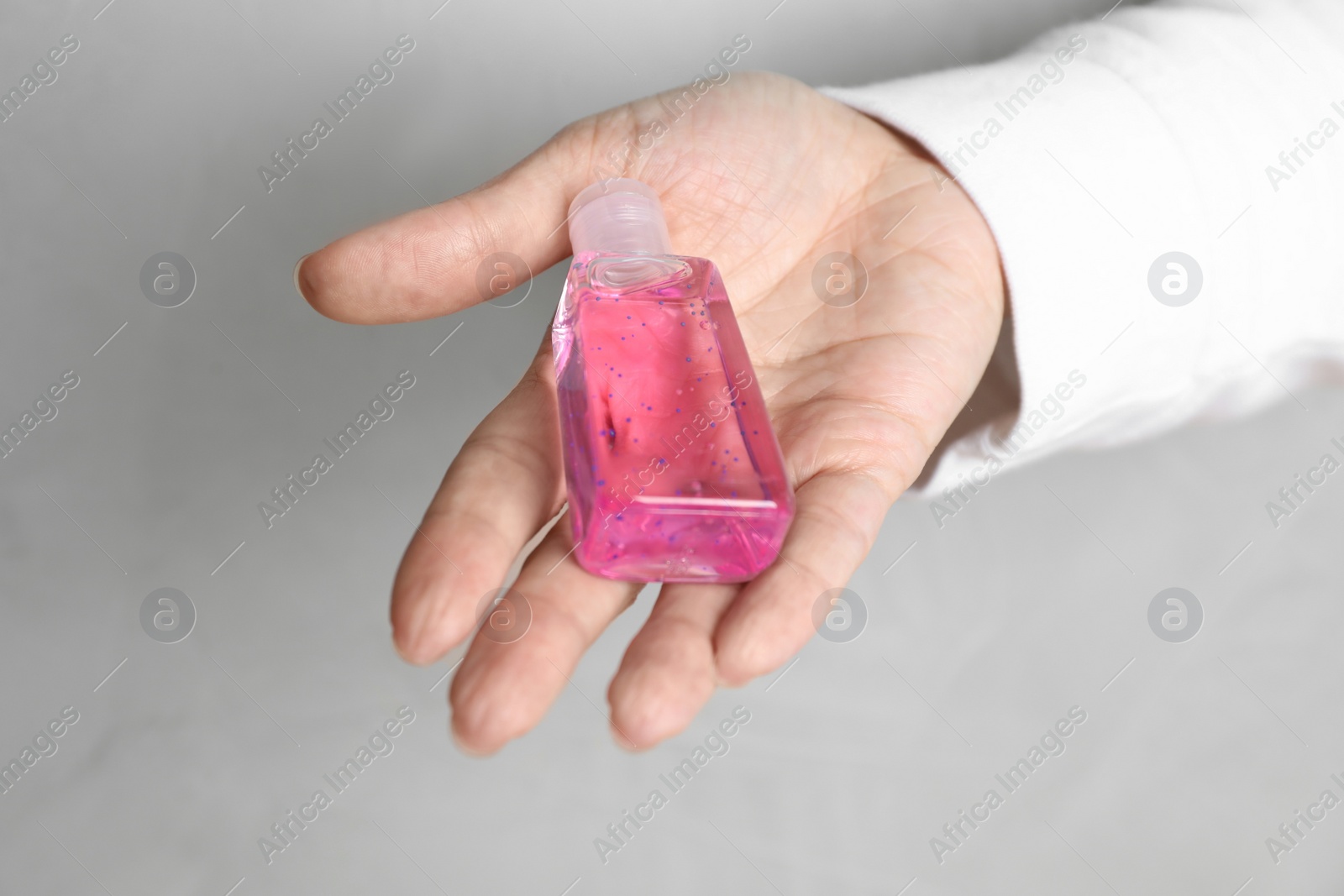 Photo of Woman holding antiseptic gel on light grey background, closeup