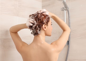 Young woman washing her hair with shampoo in shower, back view