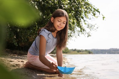 Cute little girl playing with paper boat near river