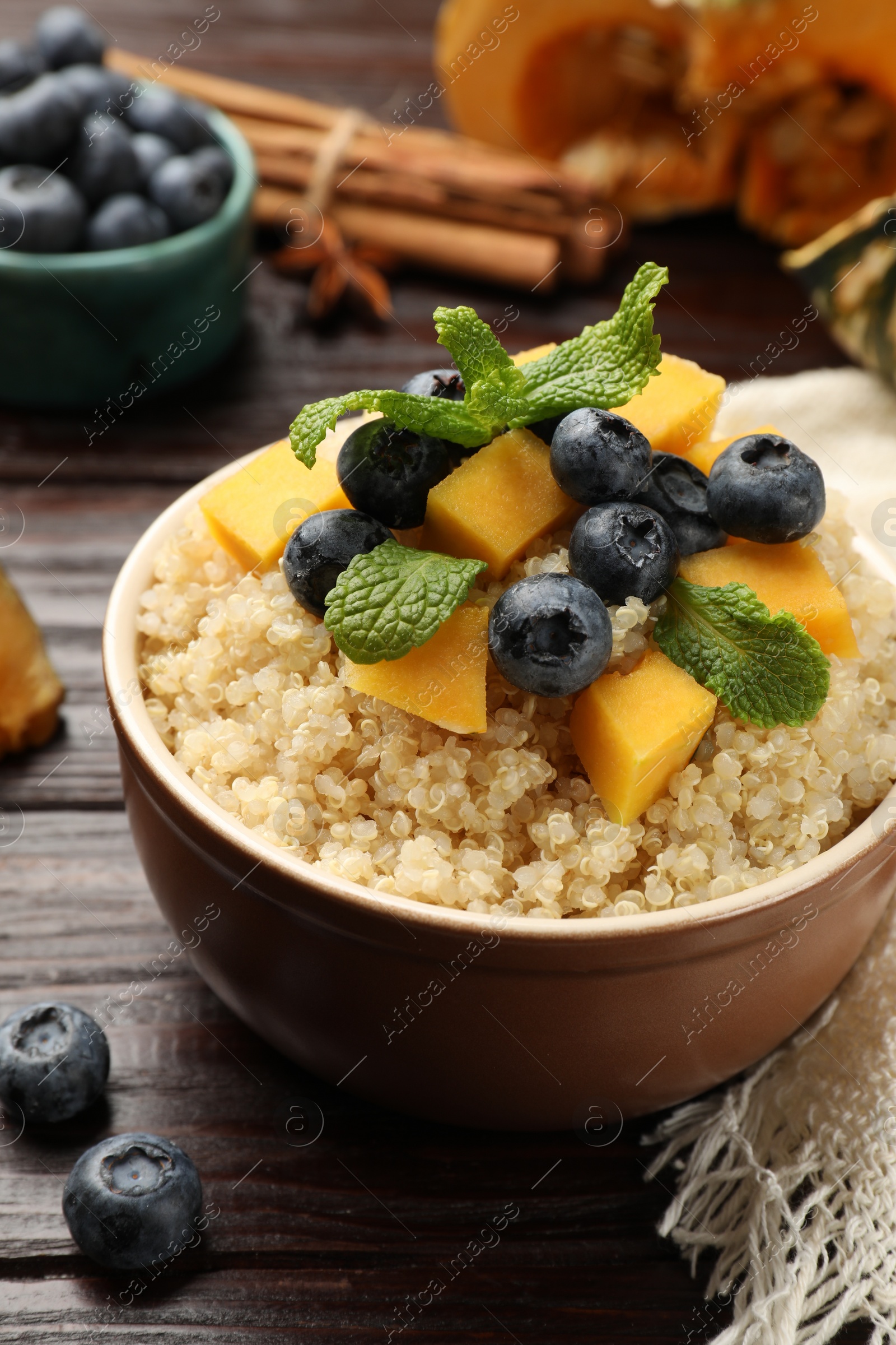 Photo of Tasty quinoa porridge with blueberries, pumpkin and mint in bowl on wooden table, closeup