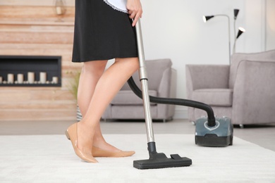 Photo of Young chambermaid removing dirt from carpet with vacuum cleaner in hotel room, closeup