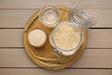 Photo of Leaven, ears of wheat and water on beige wooden table, top view