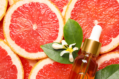 Photo of Bottle of citrus essential oil and flower on pile of grapefruit slices, flat lay. Space for text