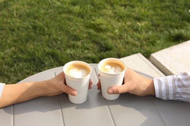 Coffee to go. Couple with paper cups at grey table outdoors, closeup