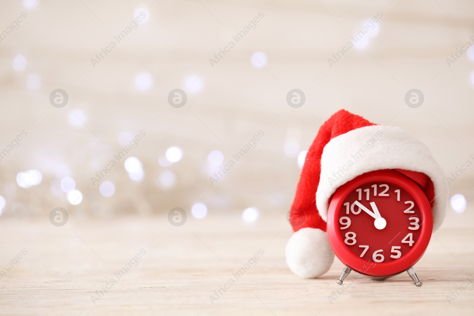 Photo of Alarm clock with decor on white wooden table against blurred Christmas lights. New Year countdown