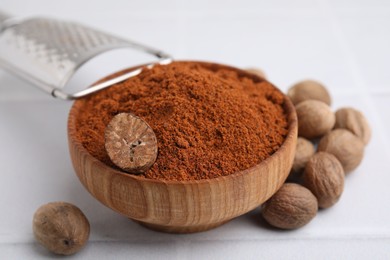 Photo of Nutmeg powder in bowl and seeds on white table, closeup