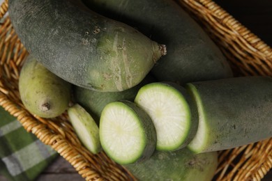 Green daikon radishes in wicker basket on wooden table, top view