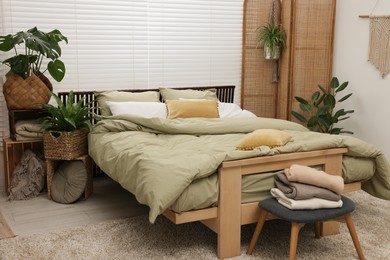 Comfortable bed and beautiful green houseplants in bedroom