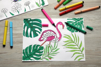 Photo of Coloring pages with children drawings and set of felt tip pens on wooden table, flat lay