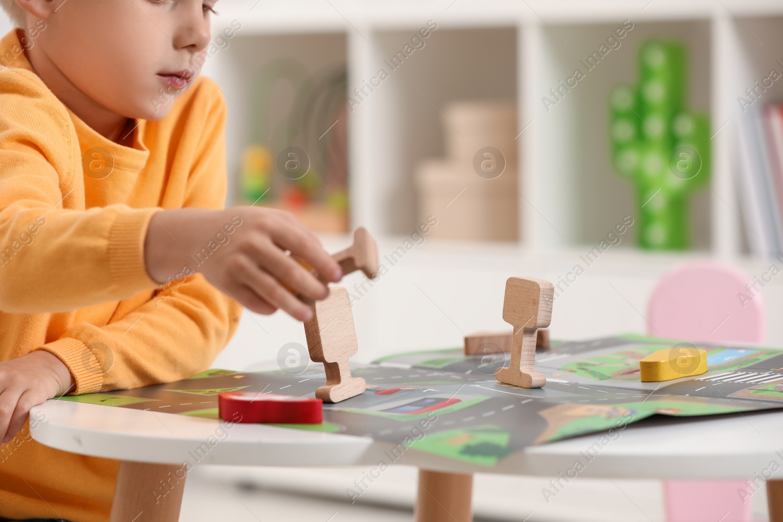 Photo of Little boy playing with set of wooden road signs and cars at table indoors, closeup. Child's toy