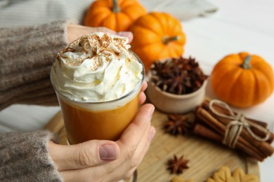 Photo of Woman holding cup of tasty pumpkin spice latte with whipped cream at white table, closeup