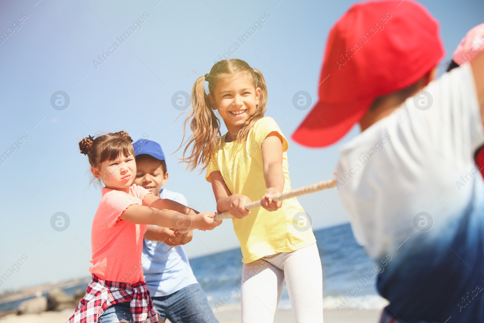 Photo of Cute children pulling rope during tug of war game on beach. Summer camp