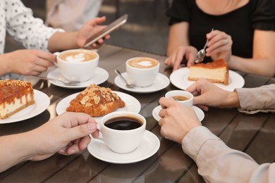 Photo of Friends drinking coffee at wooden table in outdoor cafe, closeup