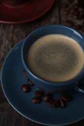 Cup of delicious coffee and beans on wooden table, closeup