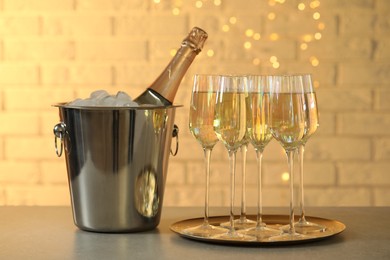 Glasses of champagne and ice bucket with bottle on grey table