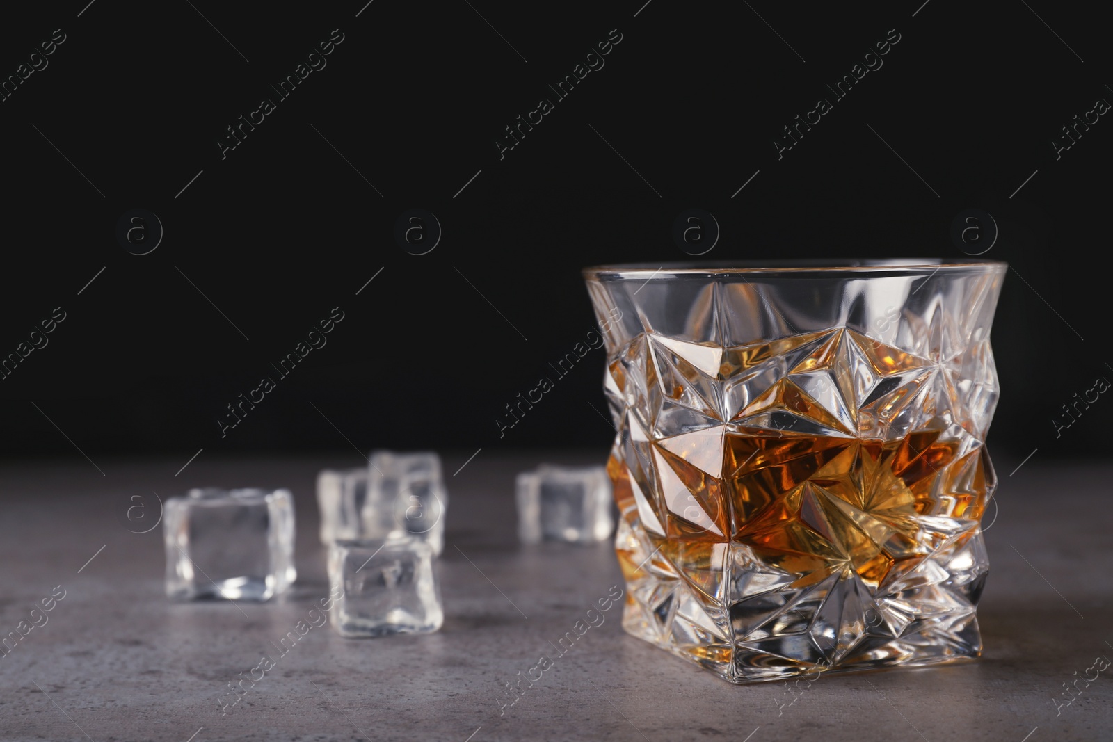 Photo of Golden whiskey in glass with ice cubes on table. Space for text