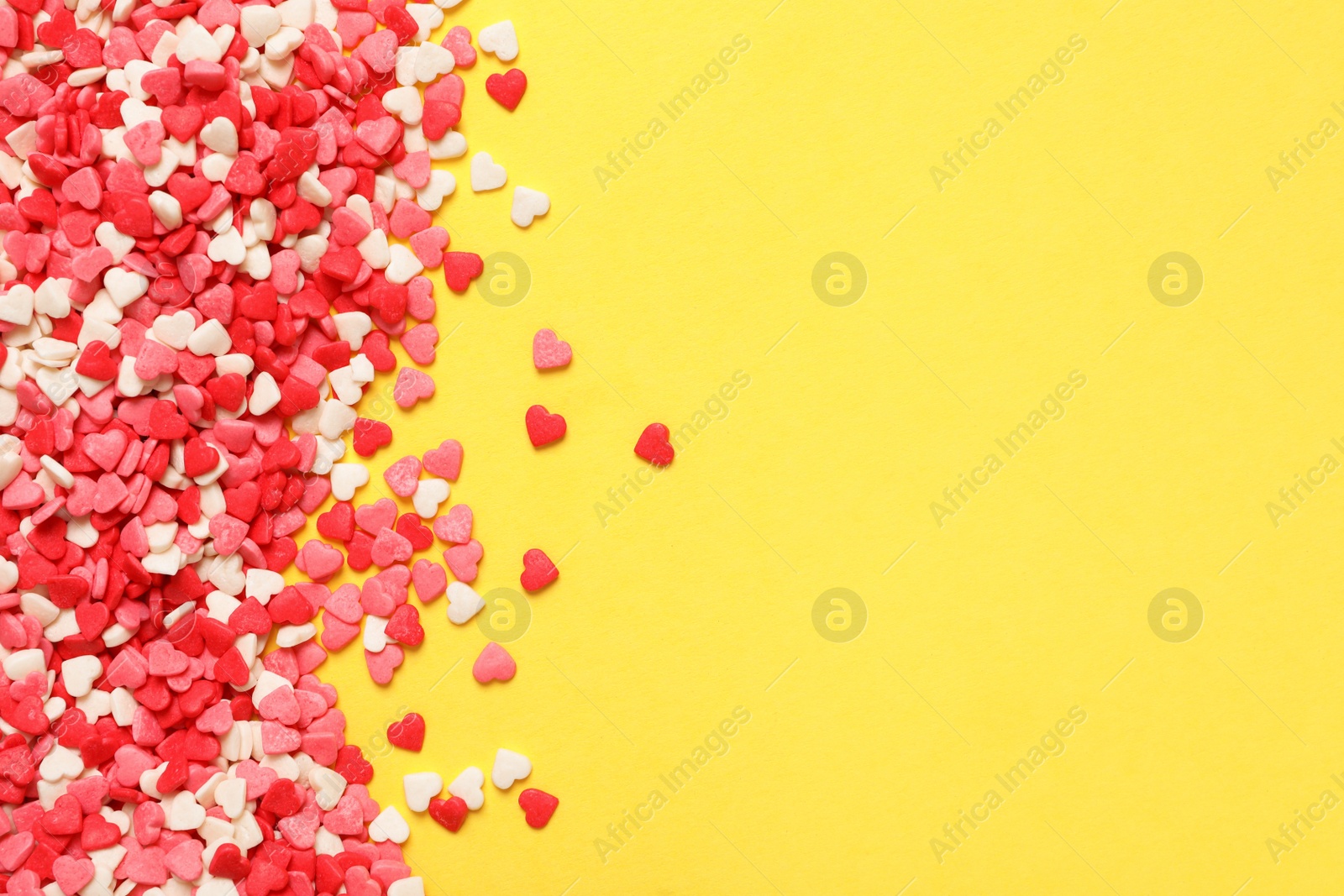 Photo of Bright heart shaped sprinkles on yellow background, flat lay. Space for text