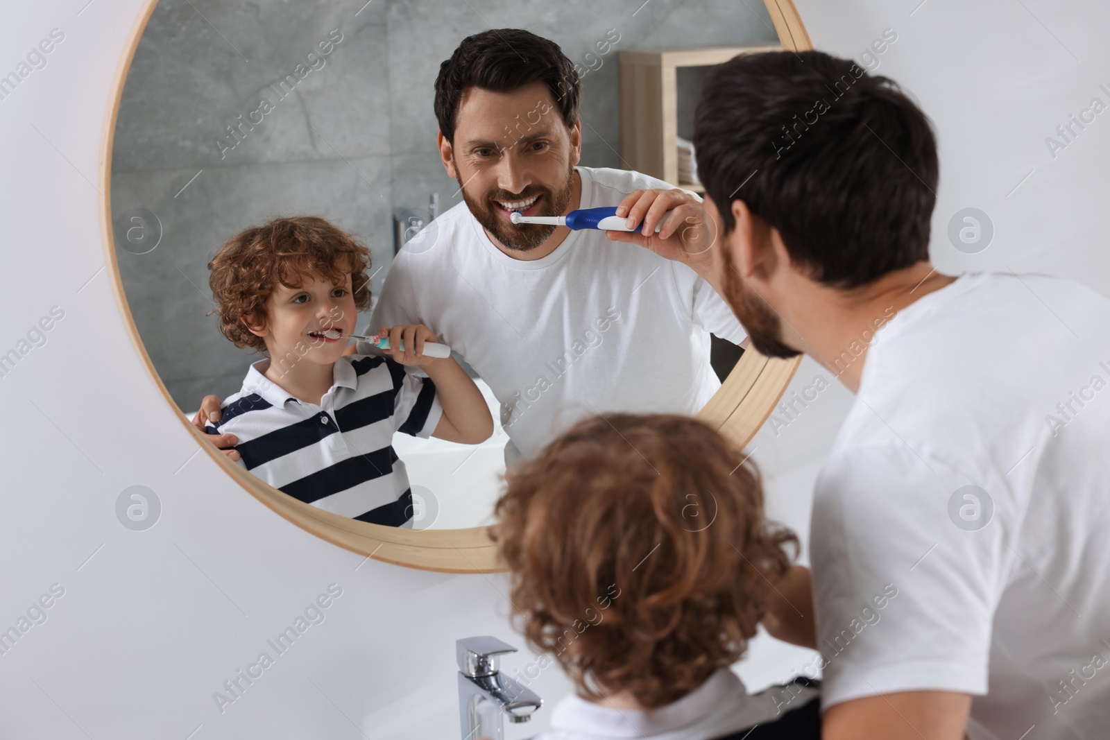 Photo of Father and his son brushing teeth together near mirror in bathroom