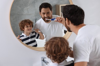 Photo of Father and his son brushing teeth together near mirror in bathroom