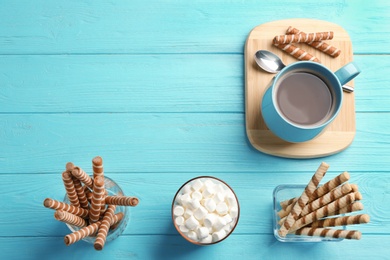 Chocolate wafer rolls, marshmallows and cup of cocoa on wooden background, top view with space for text