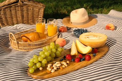 Picnic blanket with delicious food and juice on green grass outdoors