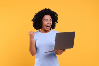 Emotional young woman with laptop on yellow background