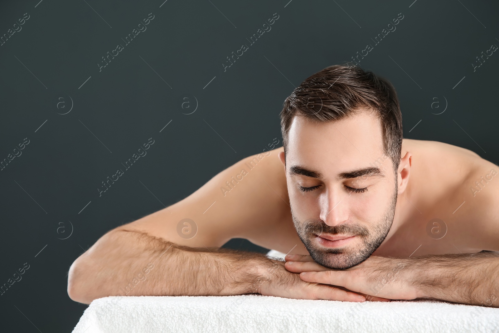 Photo of Handsome man relaxing on massage table against black background, space for text. Spa service