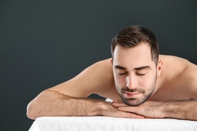 Handsome man relaxing on massage table against black background, space for text. Spa service