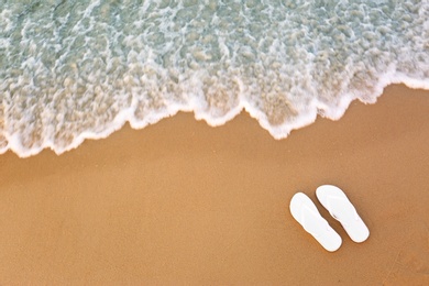 Photo of White flip flops on sand near sea, top view with space for text. Beach accessories