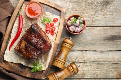 Piece of baked pork belly served with sauce and chili pepper on wooden table, flat lay. Space for text