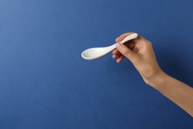 Woman holding empty miso soup spoon on color background, closeup. Space for text