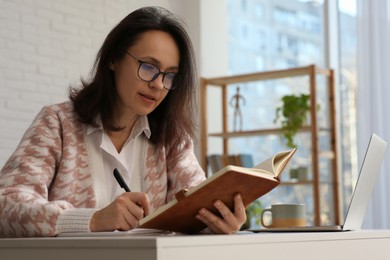 Woman with modern laptop and notebook learning at home