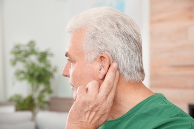 Photo of Mature man adjusting hearing aid at home