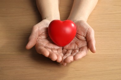 Photo of Elderly woman holding red heart in hands at wooden table, closeup