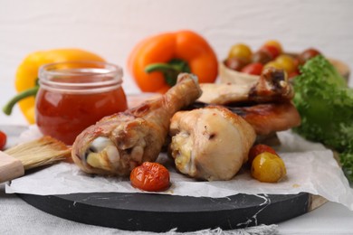 Photo of Marinade, basting brush, roasted chicken drumsticks and tomatoes on table