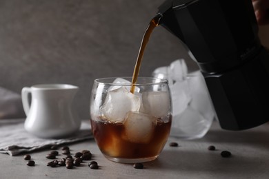 Photo of Woman pouring coffee into glass with ice cubes at gray table, closeup