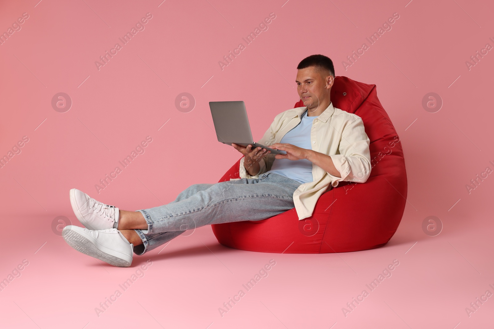 Photo of Handsome man with laptop on red bean bag chair against pink background