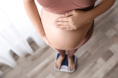 Photo of Pregnant woman standing on scales indoors, above view