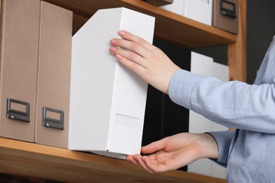 Photo of Woman taking folder with documents from shelf in office, closeup