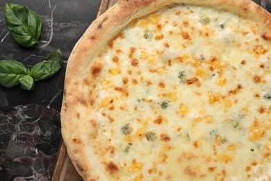 Photo of Delicious cheese pizza and basil on black marble table, flat lay