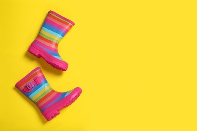 Photo of Striped rubber boots on yellow background, top view. Space for text
