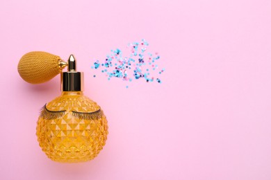 Photo of Perfume bottle with false eyelashes spraying shiny confetti on pink background, flat lay. Space for text