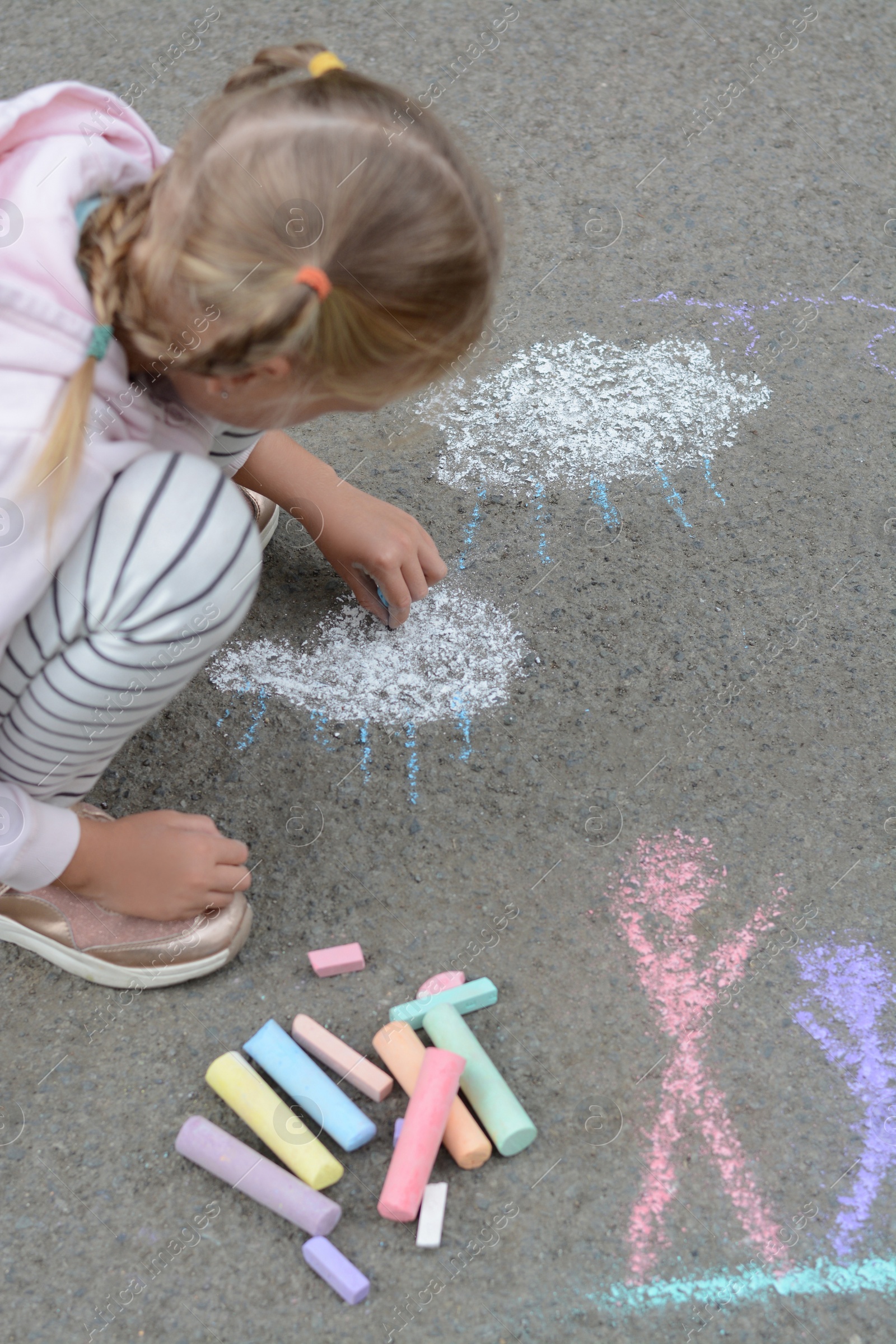 Photo of Little child drawing white clouds with chalk on asphalt