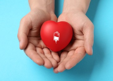 Image of Man holding red heart in hands on light blue background, top view. Blood donation concept